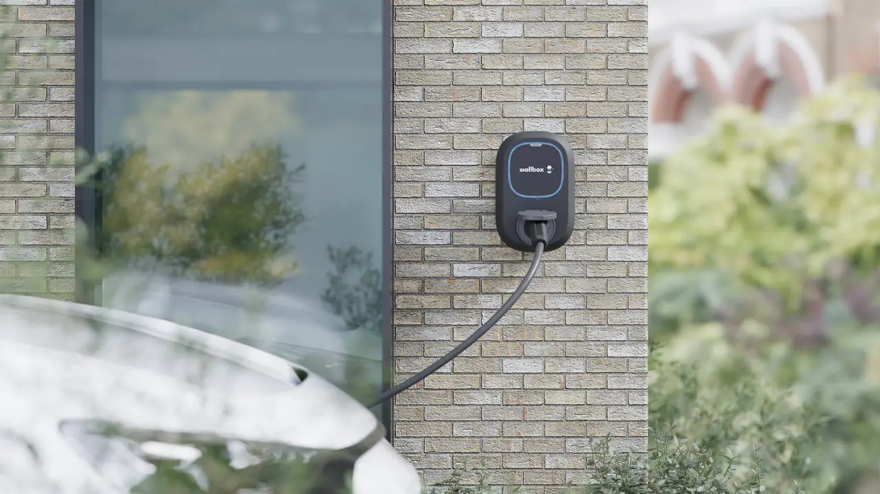 Wallbox Pulsar Plus aan de bakstenen gevel van een woning, met de laadkabel in de auto